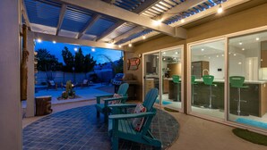 Ein überdachter Patio-Bereich mit Gartenmöbeln, einem Grill und Blick auf den Garten.