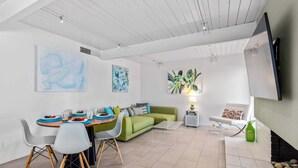 Ein modernes Wohnzimmer mit Essbereich, einem grünen Sofa, einem Flachbildfernseher und abstrakter Wandkunst.