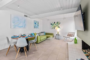 Uma sala de estar moderna com área de jantar, um sofá verde, uma TV de tela plana e arte abstrata na parede.
