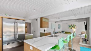 Eine moderne Küche mit einem Edelstahl-Kühlschrank, einer weißen Arbeitsplatte und grünen Barhocker.