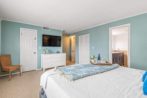 A bedroom with a bed, a dresser, a chair, a television, and a door.