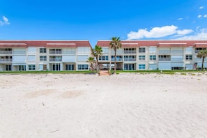A beachfront hotel with multiple balconies, a sandy beach in front, and palm trees.