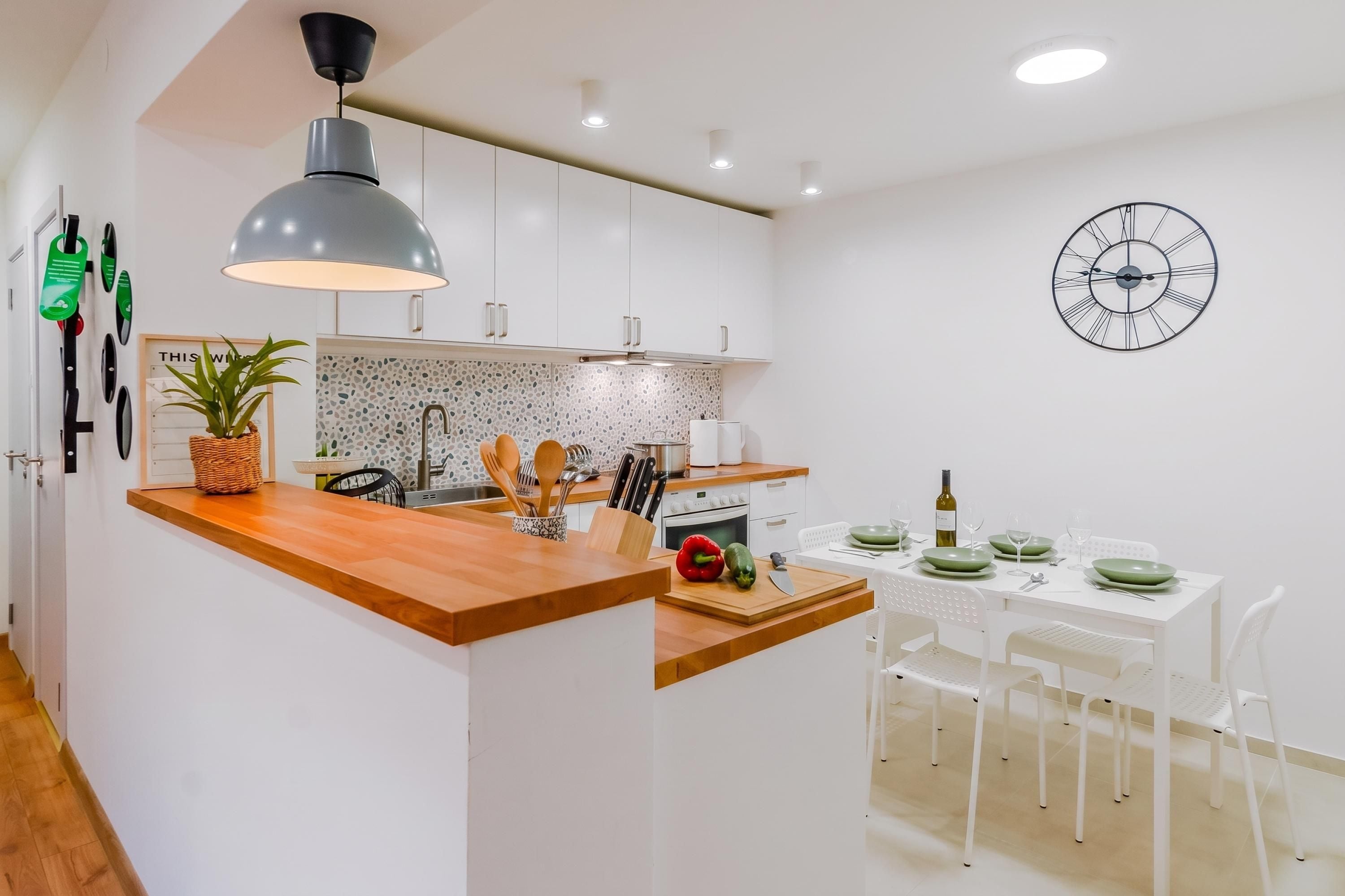 A modern kitchen with a central island, white cabinetry, a hanging light fixture, and a wall clock.