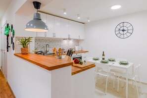 A modern kitchen with a central island, white cabinetry, a hanging light fixture, and a wall clock. - Peaceful Nest In City Center (Zagreb)