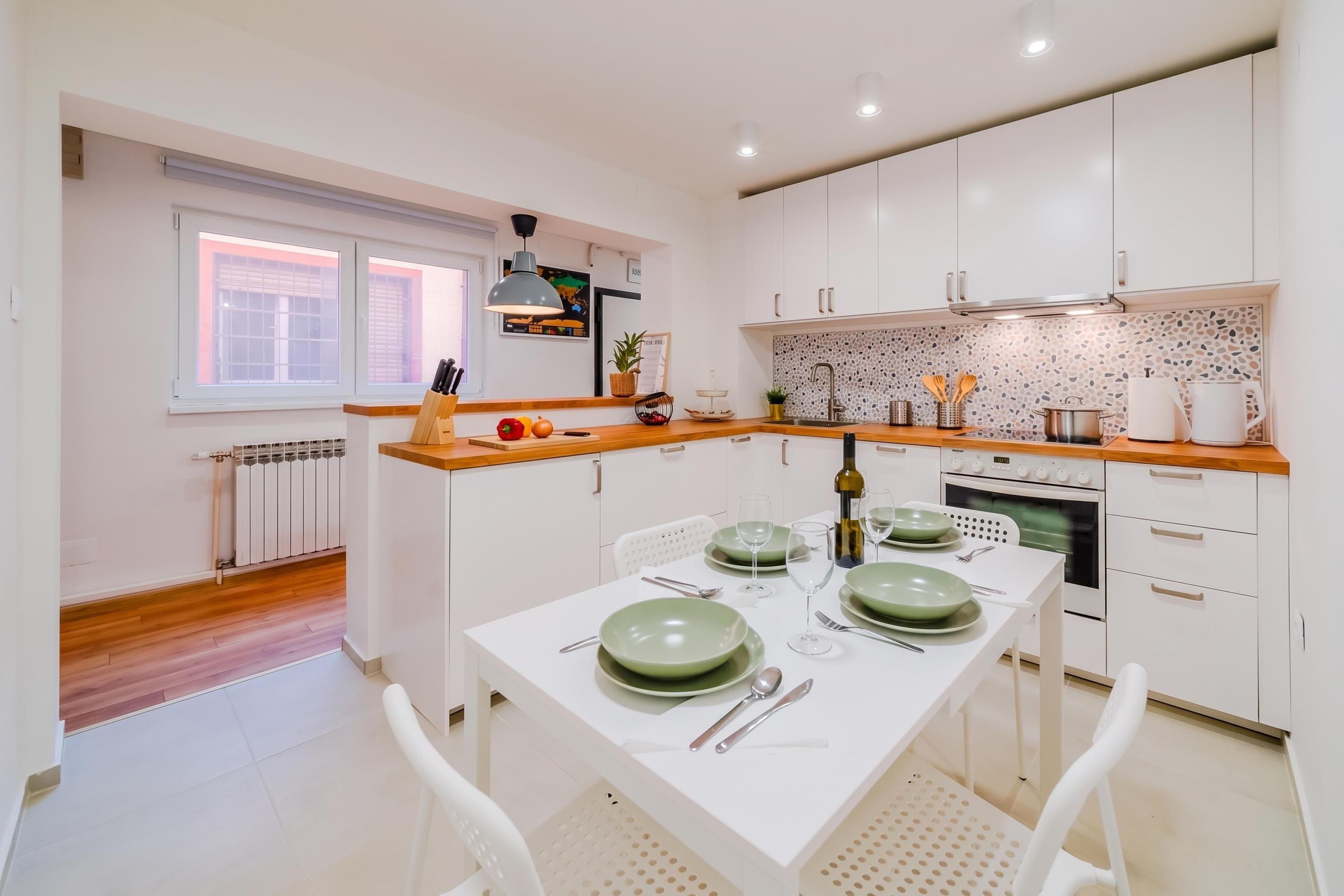 Une cuisine moderne avec des meubles blancs, un plan de travail en bois et une table à manger pour quatre personnes.