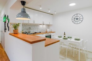 Une cuisine moderne avec un îlot central en bois, des meubles blancs, un pare-feu à motifs et une horloge murale.