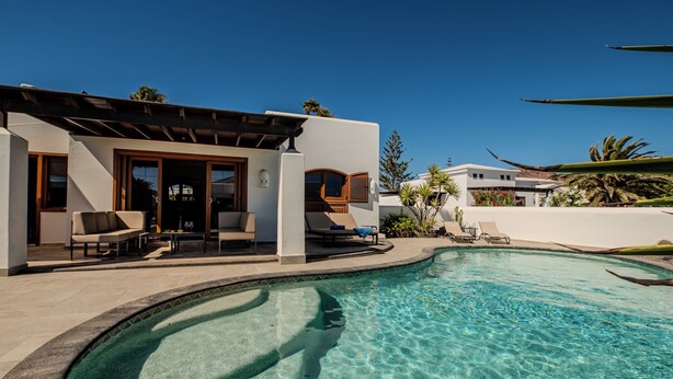 Una casa moderna con piscina, mobiliario exterior y un cielo azul despejado.