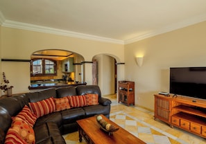 A living room with a leather sofa, wooden entertainment unit, and a flat-screen TV.