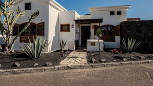 Un edificio blanco con un sendero de piedra que conduce a la entrada, rodeado de cactus y un muro de piedra.