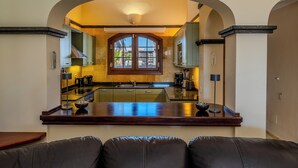 Una cocina moderna con un arco de entrada a un comedor, que cuenta con una isla central, armarios empotrados y vistas a través de un ventanal.