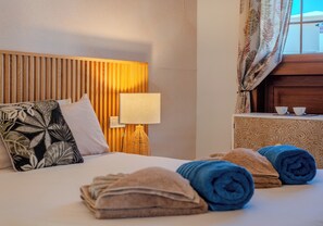 Et hotelværelse med seng, puder, lampe, sengebord og håndklæder.