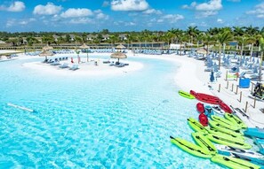 Un resort en la playa con una piscina azul cristalina, sillas de descanso y kayaks.