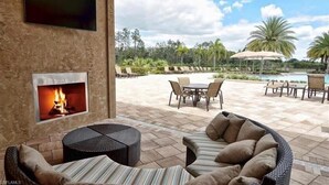Un patio al aire libre con chimenea, muebles de mimbre y un área de piscina con sillones de descanso.