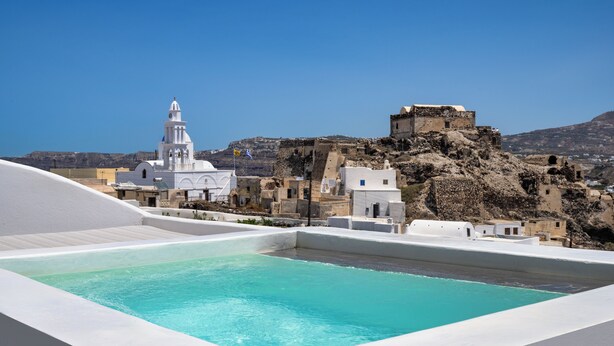A rooftop pool with a clear view of a white church and rocky hillside in the background.