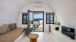 A modern living room with a sofa, a small round wooden table, a flat-screen TV, and a view of the outdoors through a glass door.