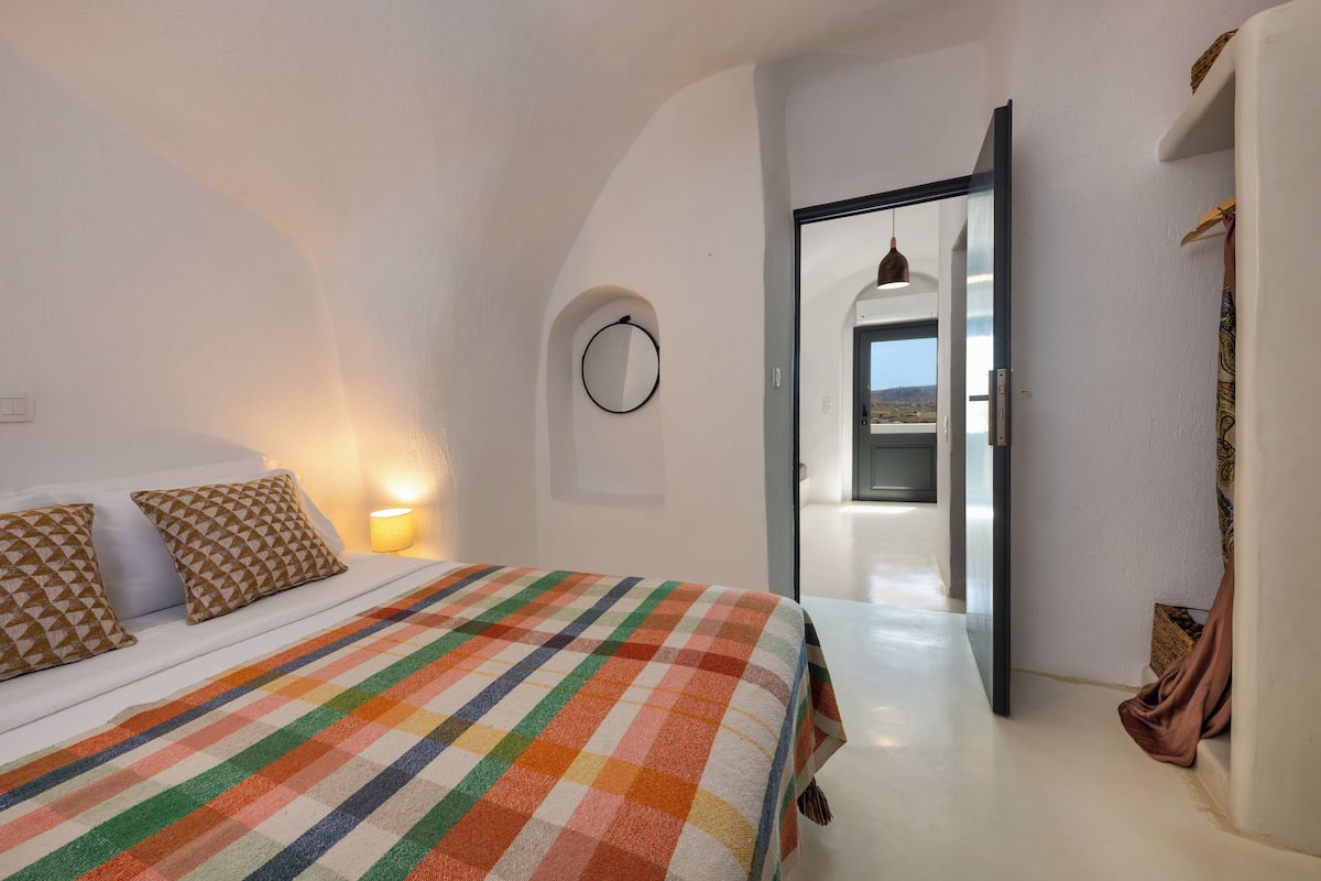 A bedroom with a checkered bedspread, a circular wall decoration, and a view of a balcony through an open door.