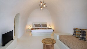 A minimalist bedroom with a bed, a TV, a small wooden stool, and a sofa.
