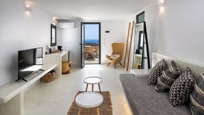 A modern living room with a TV, a sofa with patterned cushions, a small table, and a view of the outdoors through an open door.