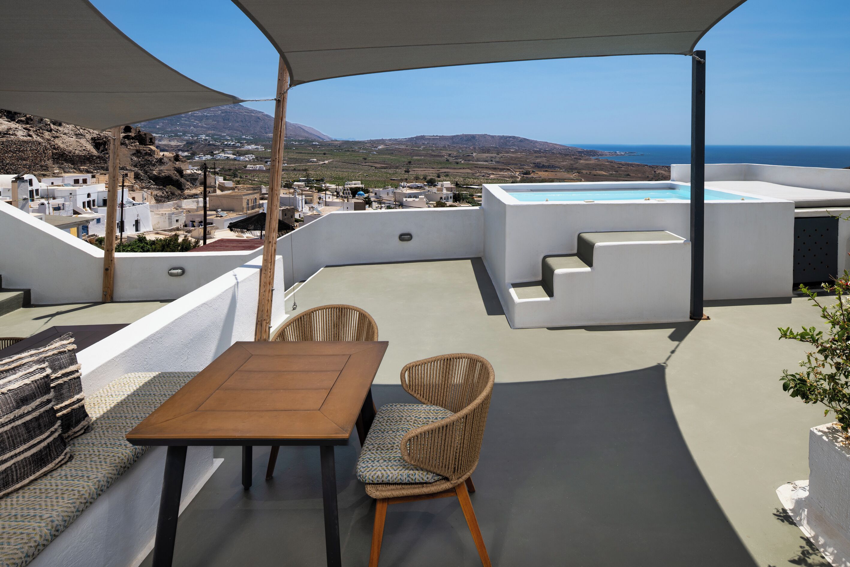 A terrace with a table and chairs, a pool, and a view of the sea and landscape.