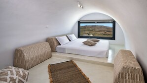 A bedroom with a bed, two sofas, a rug, and a large window with a view of a landscape.