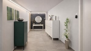 A hallway with a green cabinet, a white cabinet, a round mirror, and a vase with flowers. - Casa Armonia Sulmona Apartment (Sulmona)