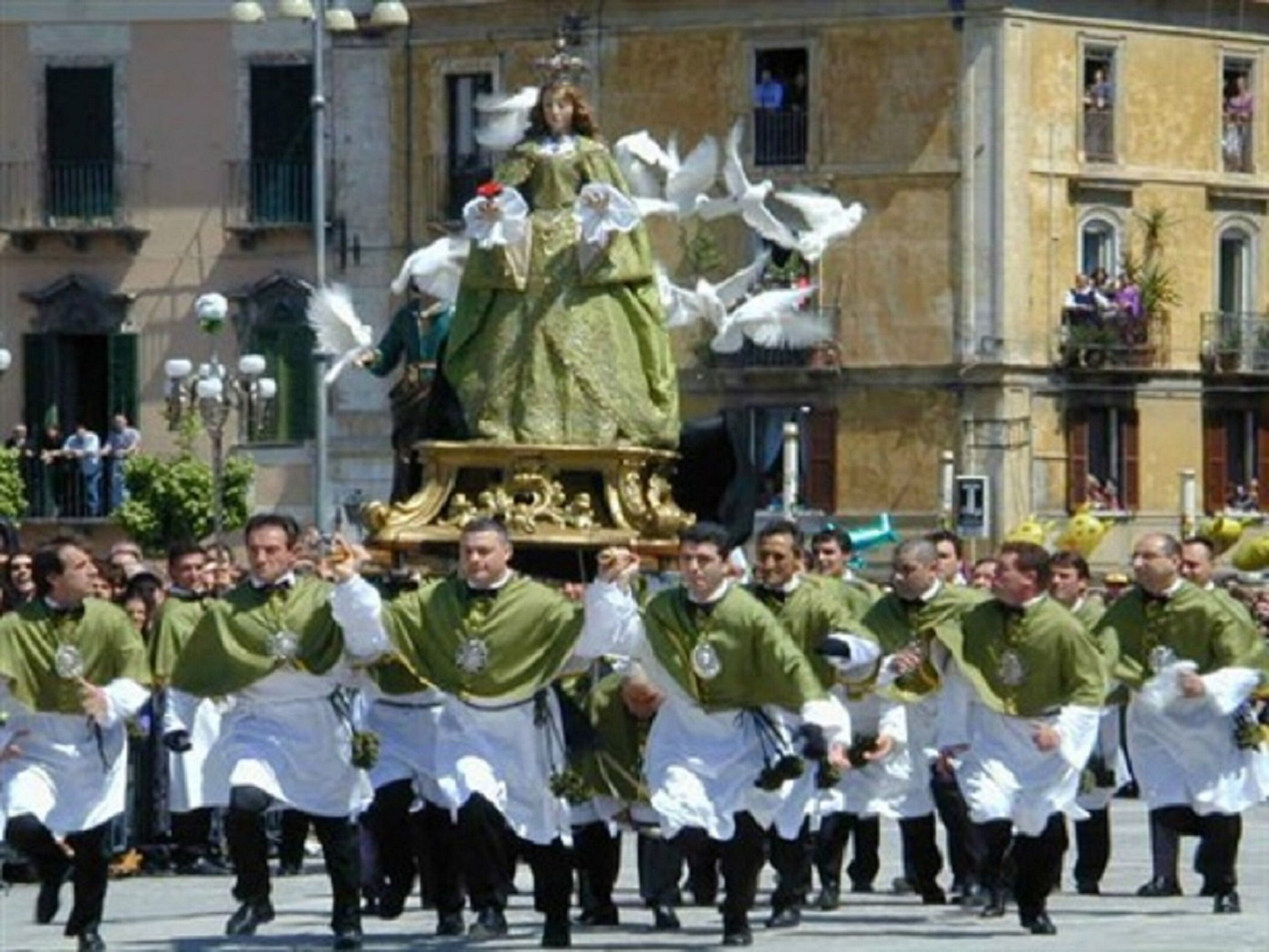 Eine Gruppe von Personen in grün-weißen Uniformen marschiert mit einer Statue einer Figur auf einer Plattform.