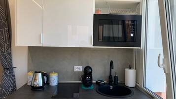 A compact kitchenette with a microwave, coffee maker, kettle, and sink.