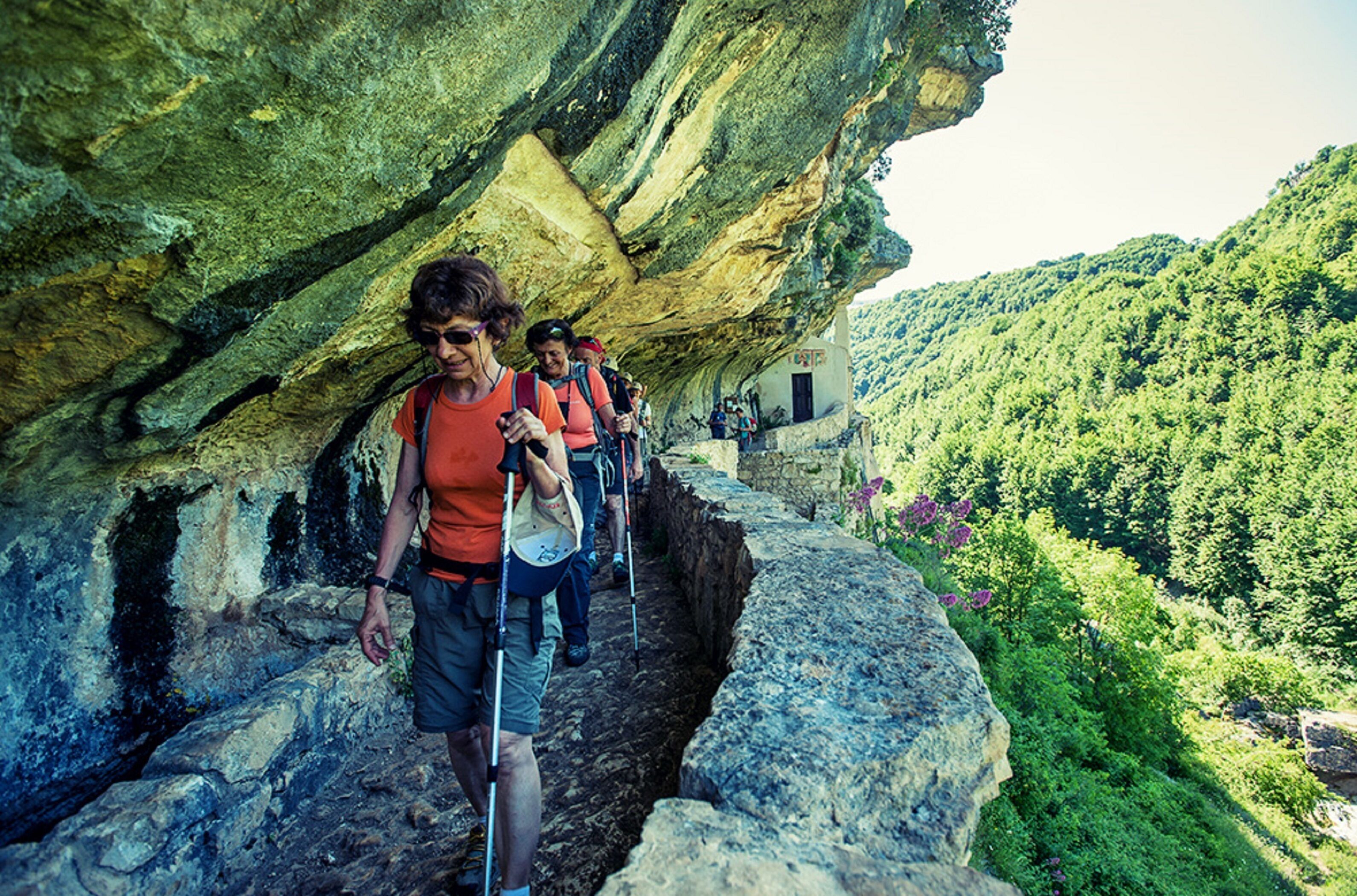 A group of hikers on a rocky path with a natural cave formation overhead.