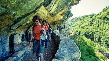 A group of hikers on a rocky path with a natural cave formation overhead.
