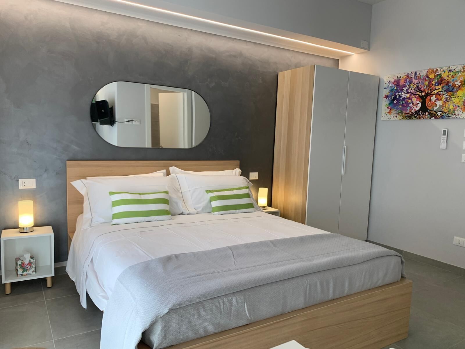 Ein modernes Schlafzimmer mit einem großen Bett, einem Spiegel, einem Kleiderschrank und einem Wandbild.