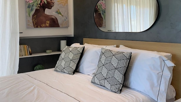 A bedroom with a bed, pillows, a painting, a mirror, and a shelf with books. - Casa Armonia Sulmona Apartment (Sulmona)
