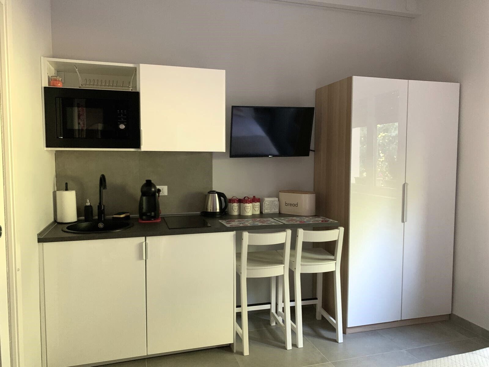 A compact kitchenette with a microwave, kettle, and toaster. There is a small table with chairs and a flat-screen TV mounted on the wall.