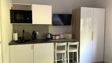 A compact kitchenette with a microwave, kettle, and toaster. There is a small table with chairs and a flat-screen TV mounted on the wall.