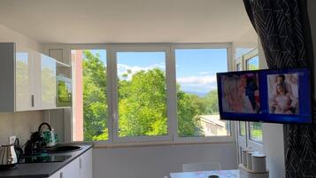 A modern kitchen with a large window, a dining area with a table, and a TV mounted on the wall.