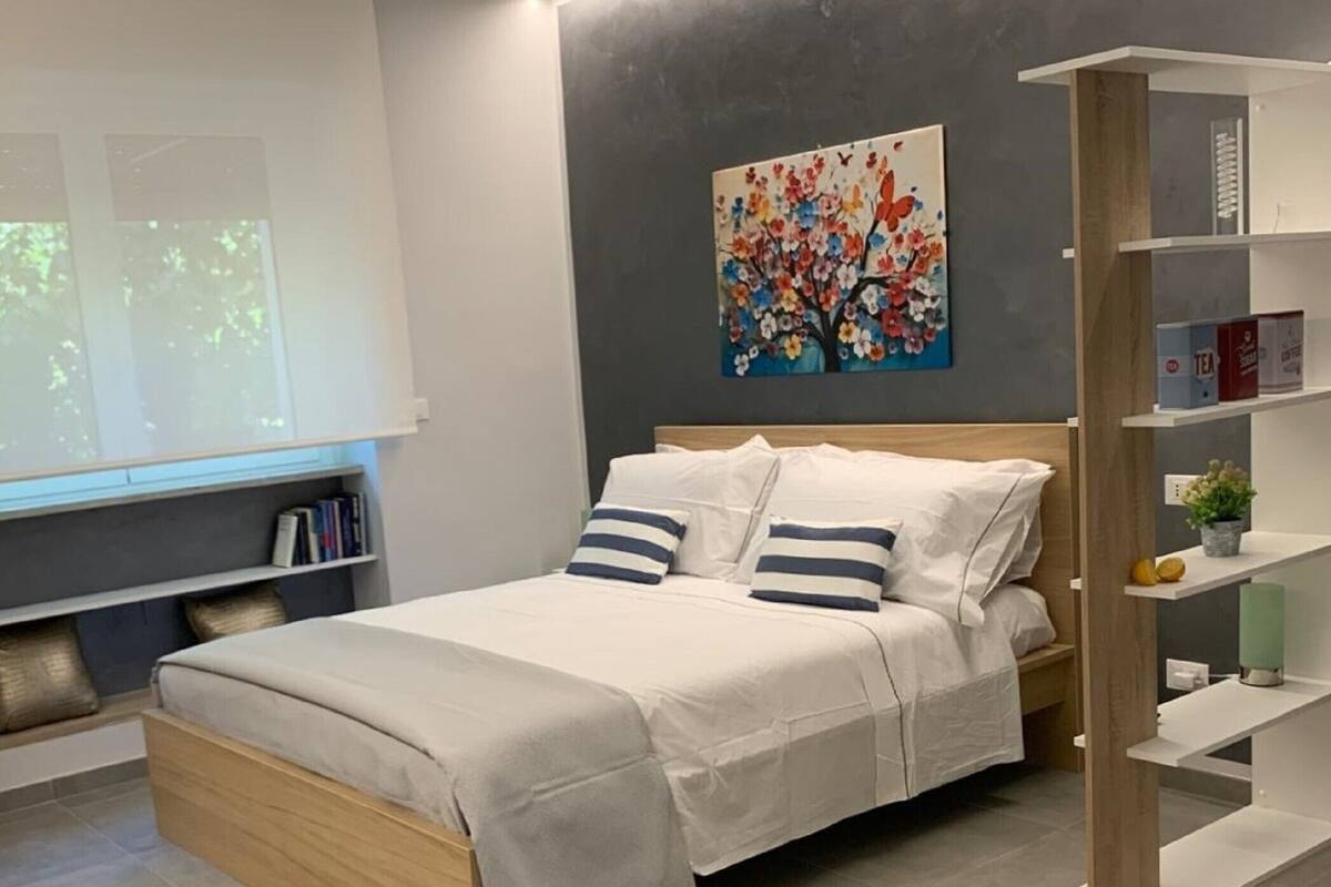 Egy modern hálószoba, amelyben található egy ágy, egy könyvespolc és egy kép a falon.