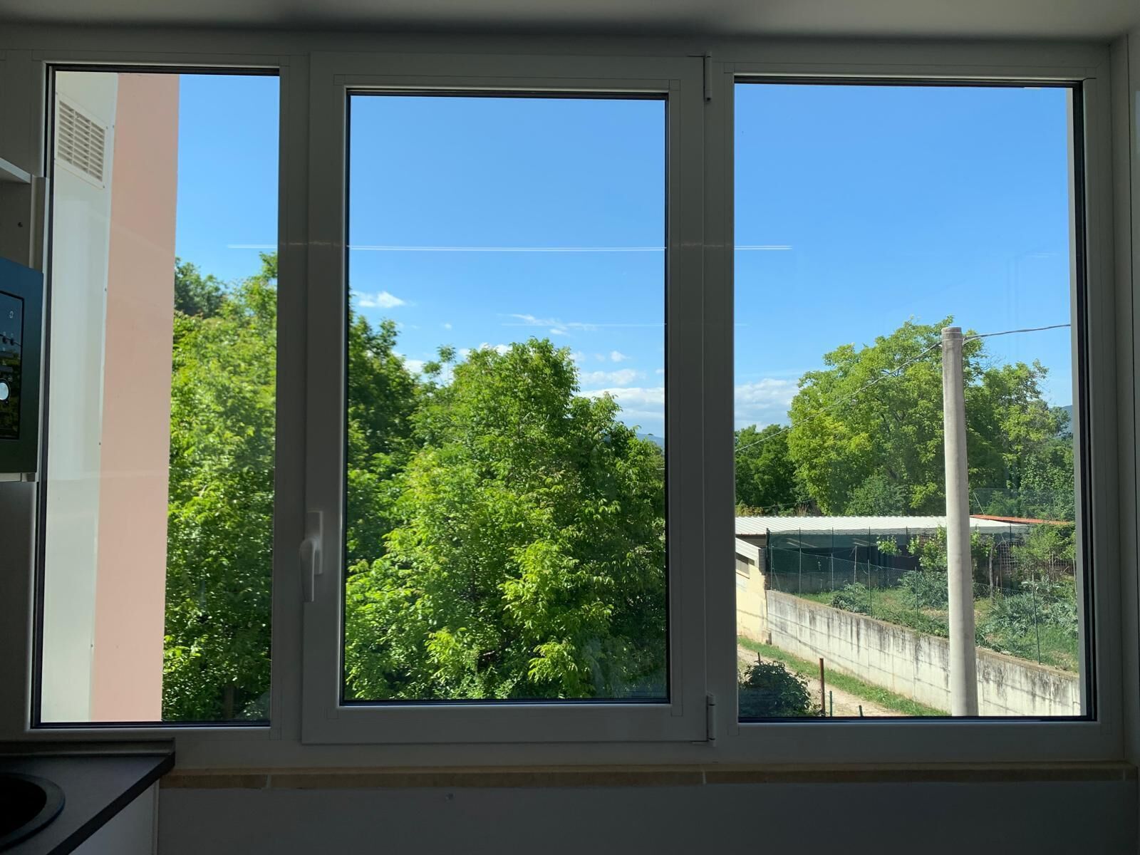 Uma janela com vista para uma paisagem verde e um céu azul límpido.