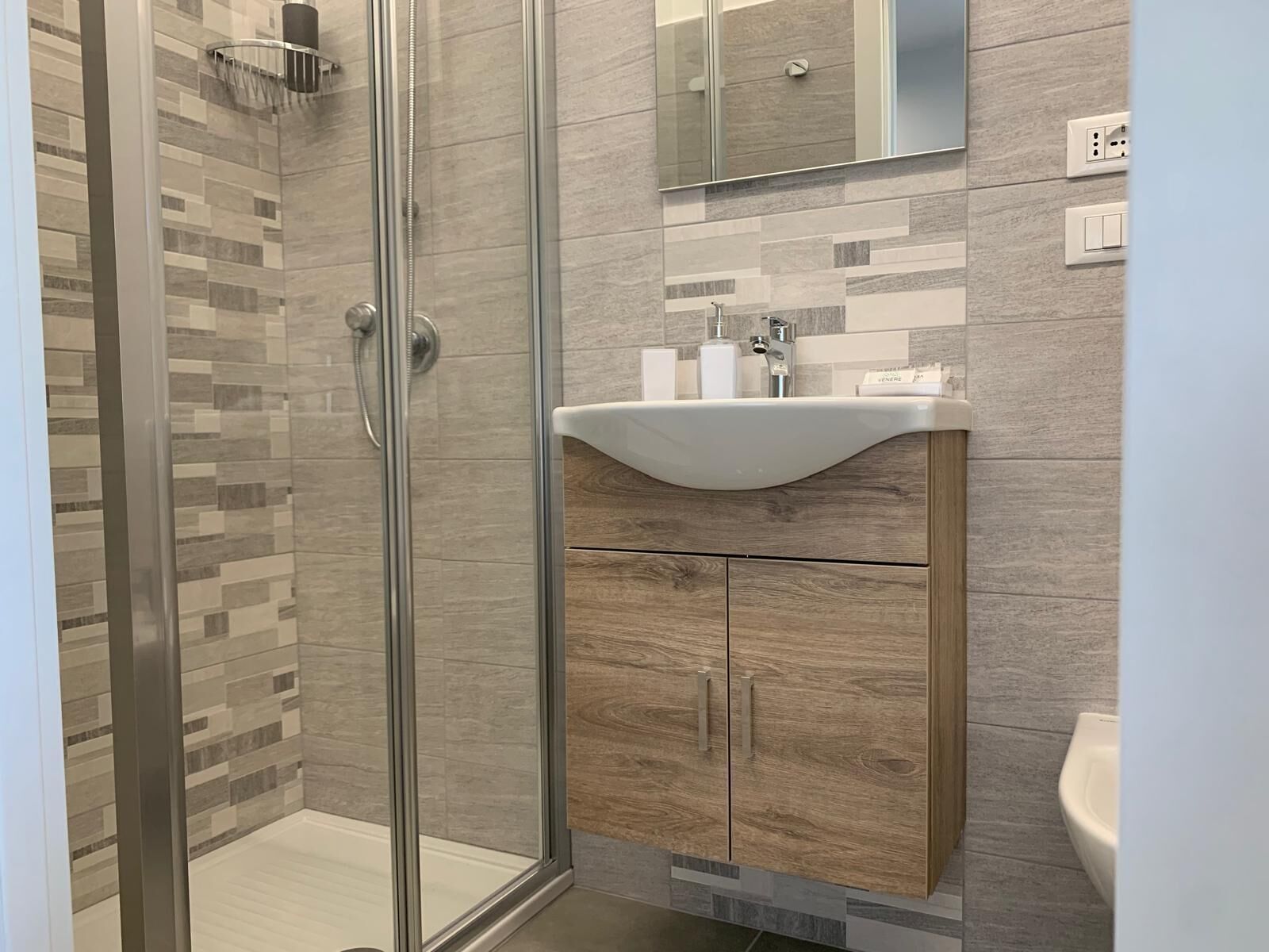 Un bagno moderno con doccia vetrata, un mobile bagno in legno con lavandino e uno specchio sopra il mobile.