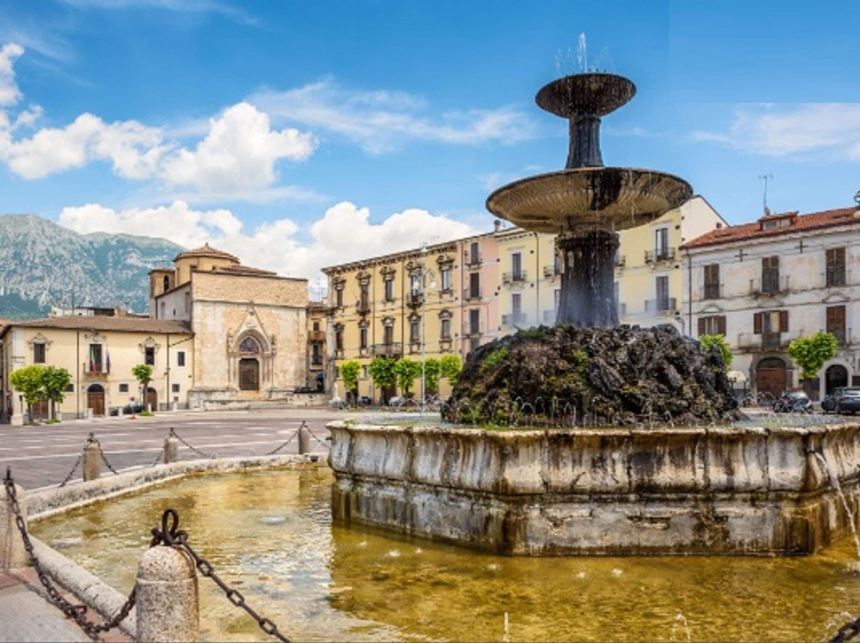 Una fuente histórica con un chorro central, rodeada por una batea de piedra y una barandilla de cadena.
