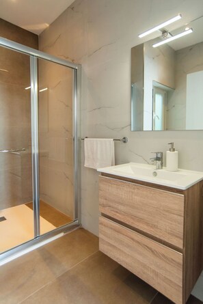 Une salle de bain moderne avec une douche à parois de verre, un lavabo blanc doté d’un meuble-vasque en bois et un miroir au-dessus du lavabo.