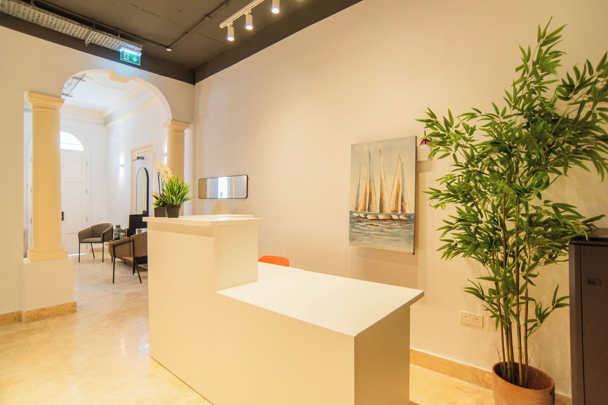 A reception area with a reception desk, chairs, a potted plant, and a painting on the wall.