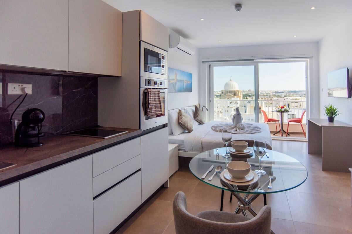 Una cucina moderna con un tavolo da pranzo in vetro, un divano letto e un balcone con vista sulla città.