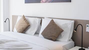 Una cama bien hecha con ropa de cama blanca y beige, una obra de arte colgada en la pared y una mesita de noche con una lámpara.