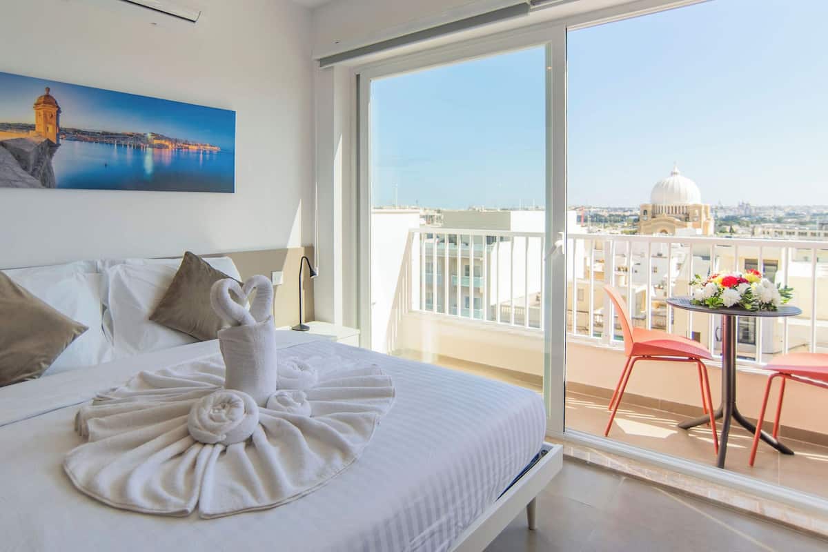 Una camera d'albergo con un letto, un quadro raffigurante una costa e un balcone con tavolo e sedie.