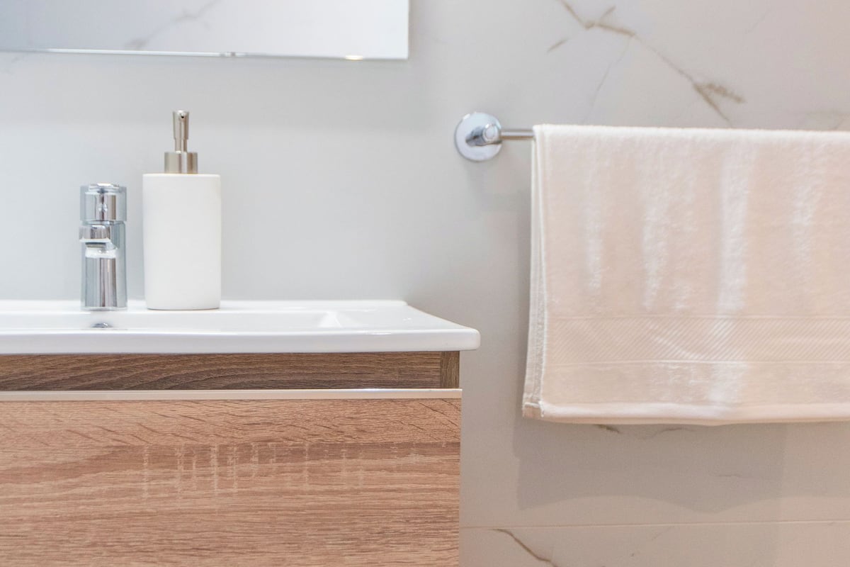 Un bagno con un mobile contenitore in legno, un lavandino bianco, uno specchio e un asciugamano appeso a un portascopevoli.