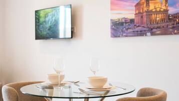 A dining area with a glass table, two chairs, and a television mounted on the wall.