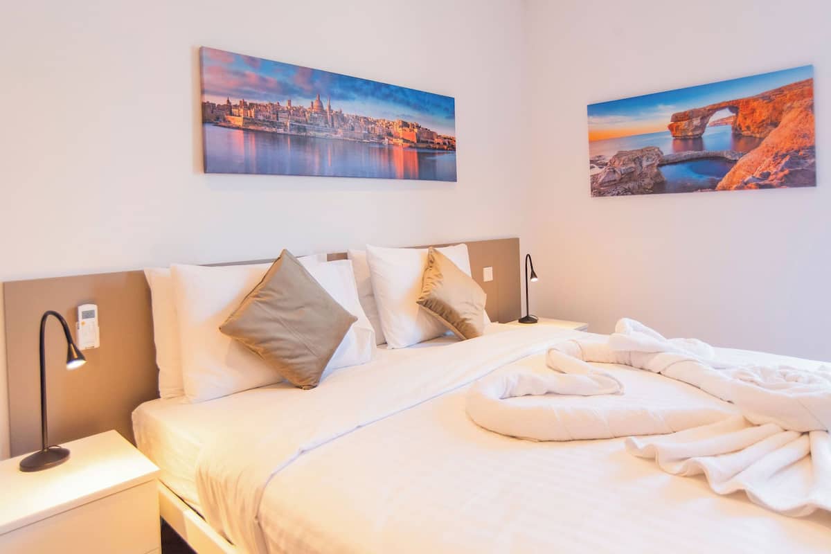 Una camera d'hotel con un letto rifatto, un comodino con una lampada e due quadri alle pareti raffiguranti paesaggi panoramici.