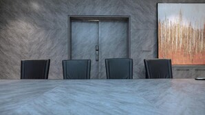 Une salle de conférence avec une table en marbre, quatre chaises, une porte et un grand tableau abstrait accroché au mur.
