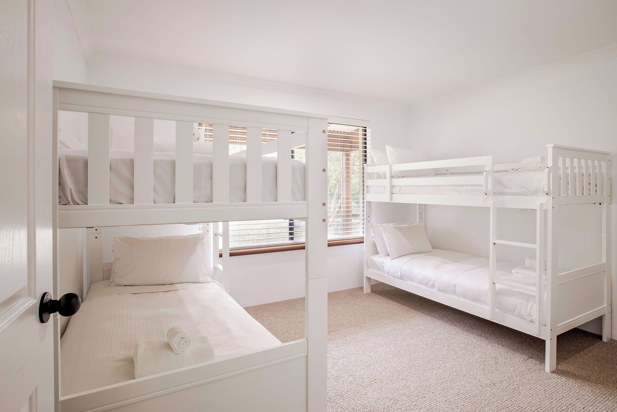 A white room with bunk beds, a door, and a window with blinds.