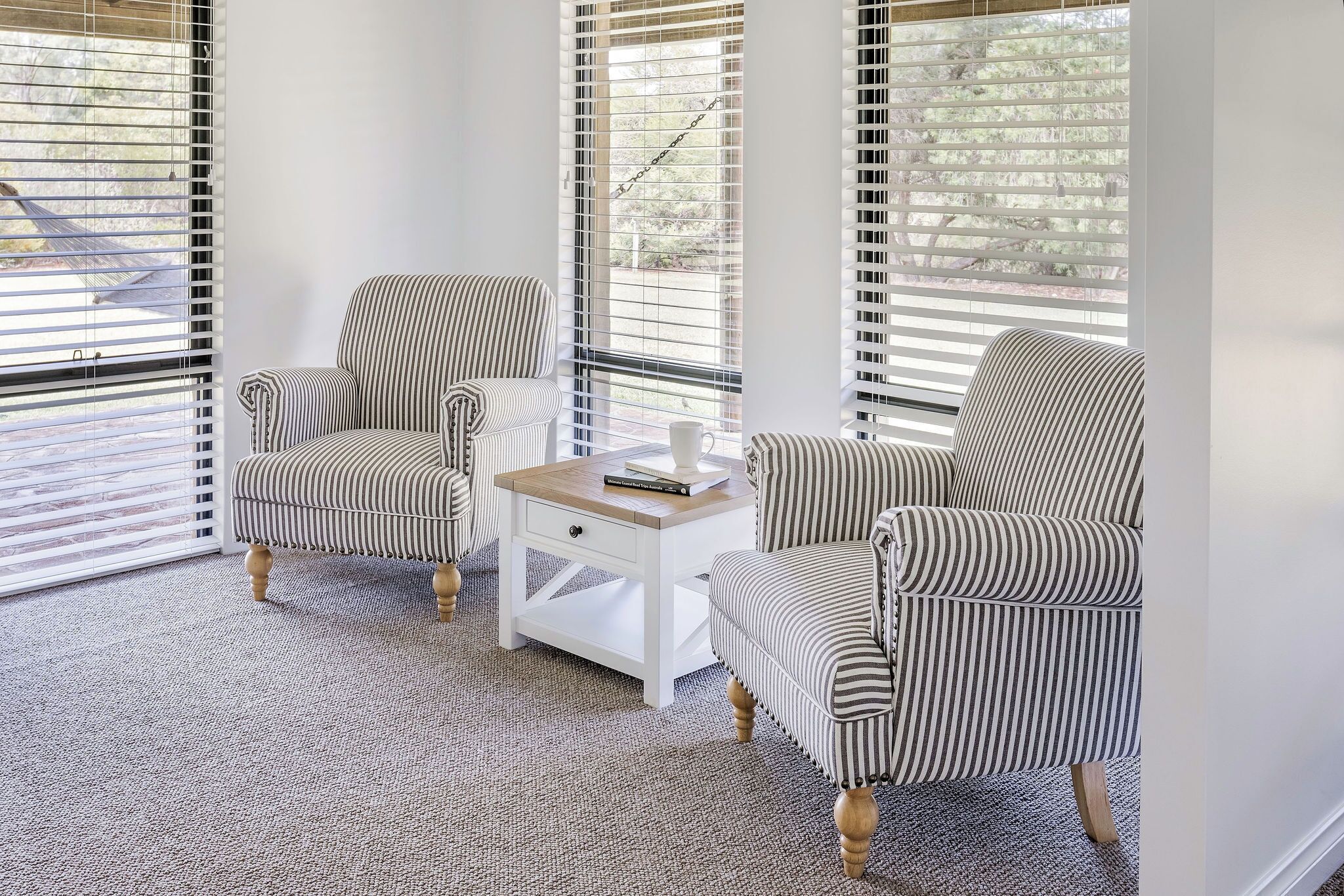 A corner seating area with two striped armchairs and a small white side table with a book and a cup.