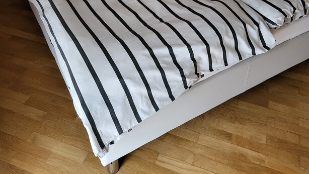 Una cama con cubrecama a rayas, una mesita redonda y una silla naranja en una habitación con piso de madera.